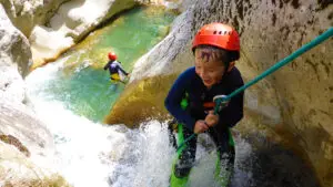 Kid enjoying abseiling down waterfalls in the Gours du Ray canyon close to Gréolières on the french riviera - Les Geckos